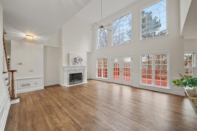 unfurnished living room with hardwood / wood-style floors, a towering ceiling, a premium fireplace, and ceiling fan