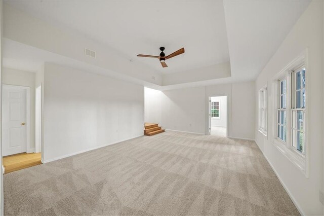 unfurnished room featuring light carpet, a tray ceiling, and ceiling fan