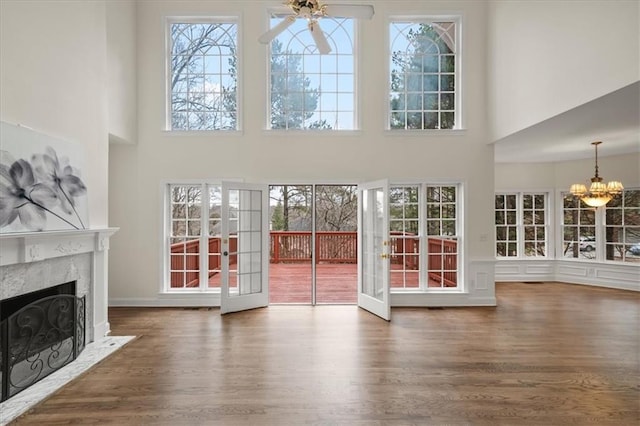 unfurnished living room with french doors, a premium fireplace, dark hardwood / wood-style flooring, and ceiling fan with notable chandelier