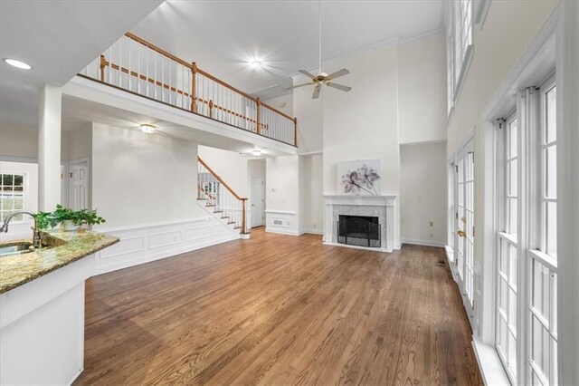 unfurnished living room featuring hardwood / wood-style flooring, sink, ceiling fan, and a towering ceiling