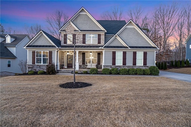 craftsman inspired home with a standing seam roof, a porch, a front lawn, and stone siding