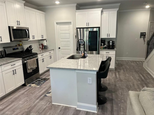 kitchen with stainless steel appliances, a sink, decorative backsplash, ornamental molding, and an island with sink