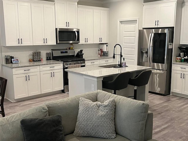 kitchen featuring stainless steel appliances, a sink, open floor plan, light wood-type flooring, and ornamental molding