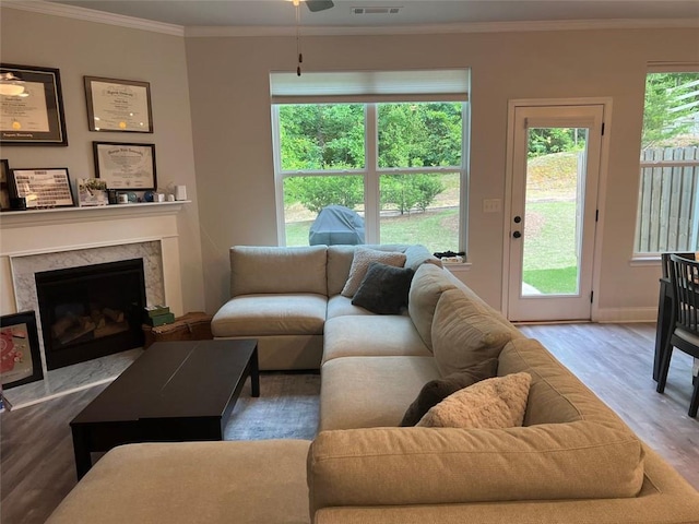 living area with wood finished floors, crown molding, ceiling fan, a premium fireplace, and baseboards