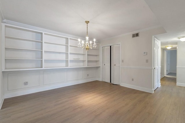 interior space featuring built in shelves, wood-type flooring, crown molding, and an inviting chandelier