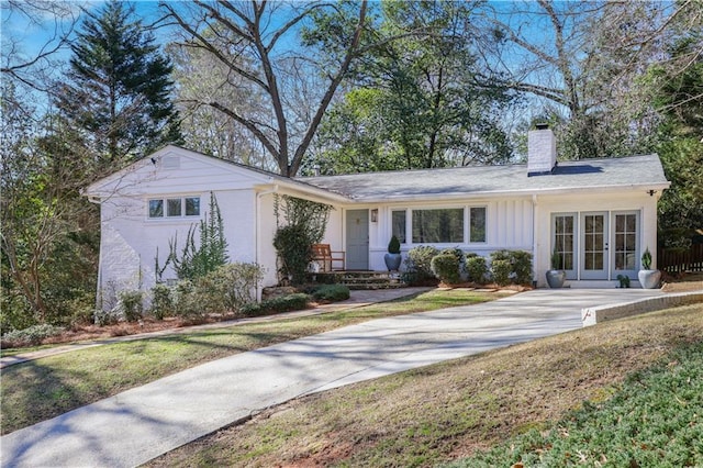 ranch-style home with board and batten siding, french doors, brick siding, and a chimney