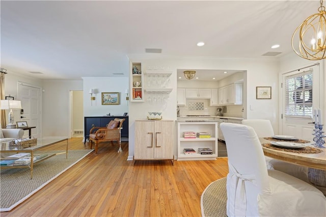 kitchen with light wood-style flooring, light countertops, ornamental molding, open shelves, and an inviting chandelier