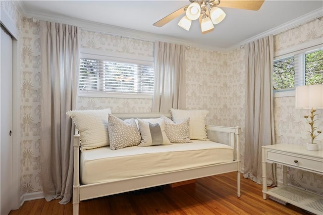 bedroom with crown molding, multiple windows, wood finished floors, and wallpapered walls