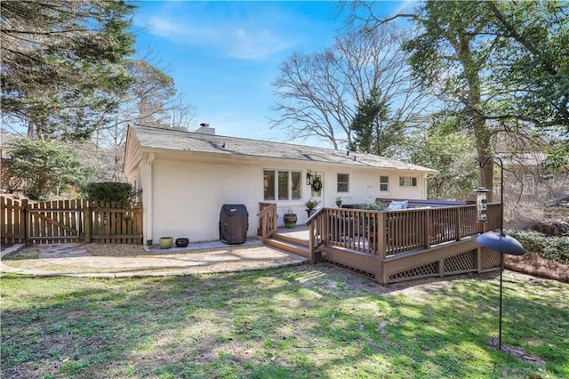 rear view of house featuring brick siding, a yard, a chimney, fence, and a wooden deck