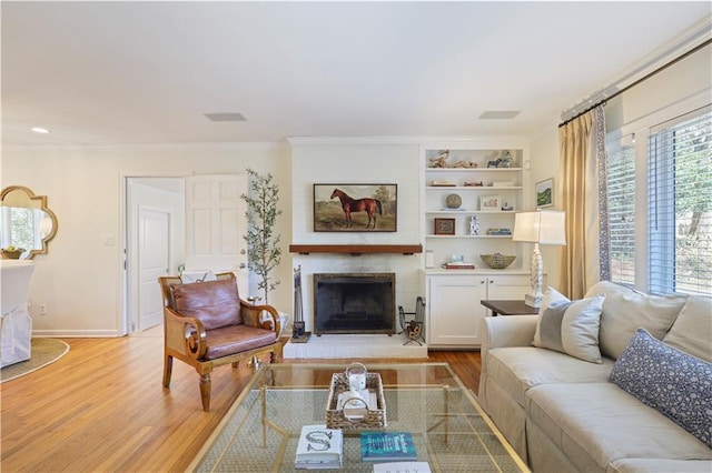 living room with light wood finished floors, baseboards, built in features, ornamental molding, and a fireplace