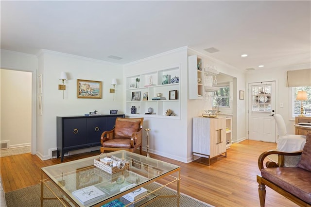 living area with built in features, visible vents, baseboards, ornamental molding, and light wood-style floors