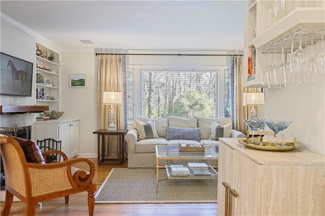 living area with a fireplace, wood finished floors, baseboards, built in features, and ornamental molding