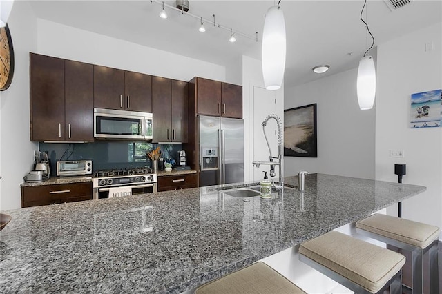 kitchen featuring a kitchen bar, hanging light fixtures, dark stone countertops, appliances with stainless steel finishes, and an island with sink