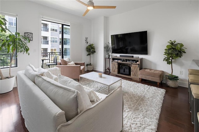 living room with dark wood-type flooring, ceiling fan, and a healthy amount of sunlight