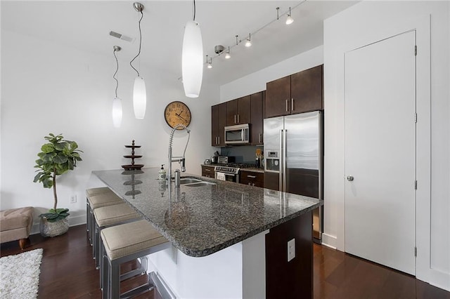 kitchen with dark wood-type flooring, hanging light fixtures, stainless steel appliances, dark brown cabinetry, and a kitchen bar