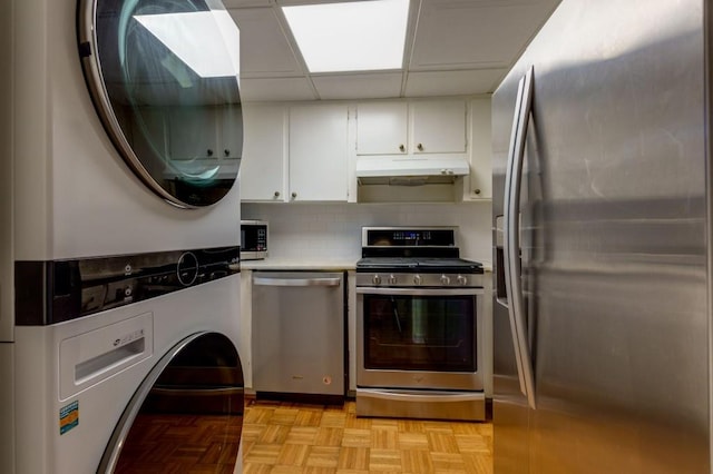 kitchen with stainless steel appliances, white cabinetry, tasteful backsplash, light parquet flooring, and stacked washing maching and dryer