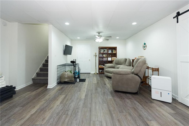 living room with ceiling fan, a barn door, a paneled ceiling, and hardwood / wood-style floors