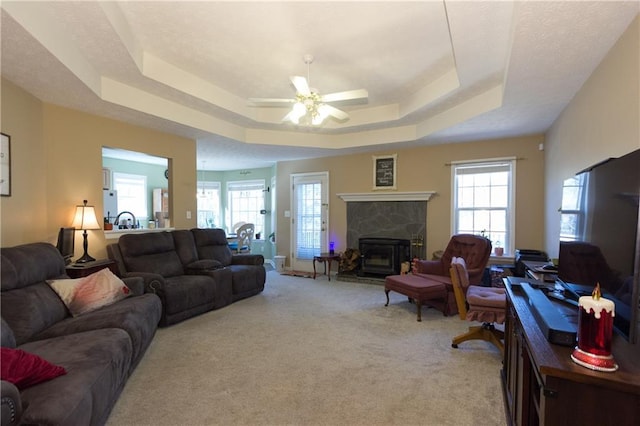 carpeted living room featuring ceiling fan, a high end fireplace, and a tray ceiling