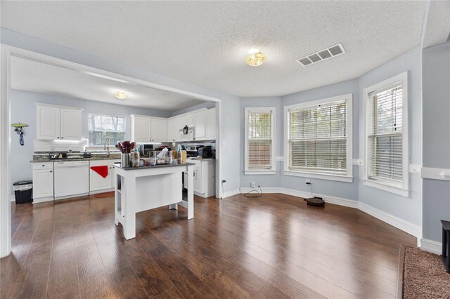 kitchen featuring a breakfast bar area, white cabinetry, dark countertops, visible vents, and white dishwasher