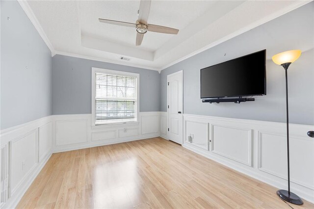 unfurnished living room featuring wainscoting, ceiling fan, light wood finished floors, visible vents, and a tray ceiling