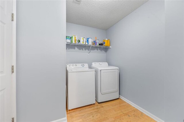 clothes washing area with washing machine and clothes dryer, laundry area, light wood-style flooring, baseboards, and a textured ceiling