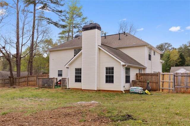 rear view of property featuring roof with shingles, a yard, a fenced backyard, and a chimney