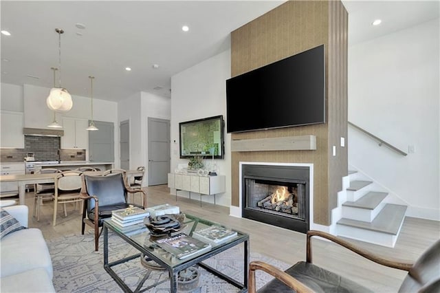 living room with light wood-type flooring, a large fireplace, a towering ceiling, and recessed lighting