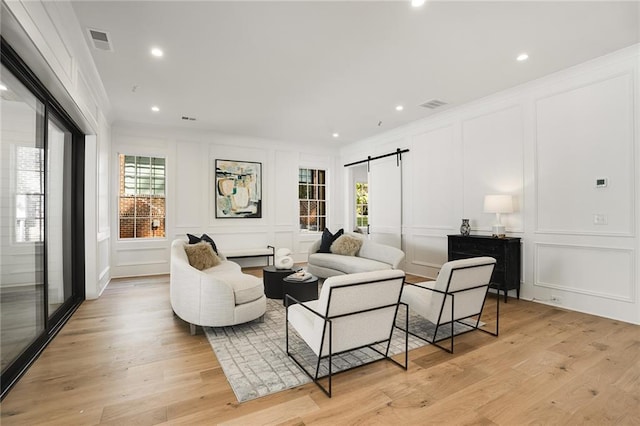 living room featuring light wood-type flooring, a barn door, and ornamental molding