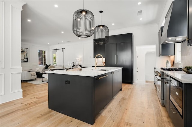 kitchen with a large island, a barn door, wall chimney range hood, and hanging light fixtures