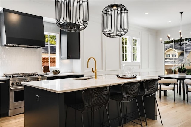 kitchen featuring stainless steel range, sink, range hood, decorative light fixtures, and a kitchen island with sink