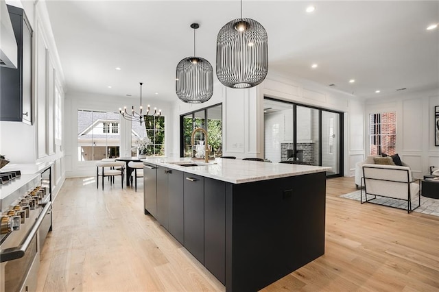 kitchen featuring pendant lighting, a large island with sink, sink, light wood-type flooring, and a notable chandelier