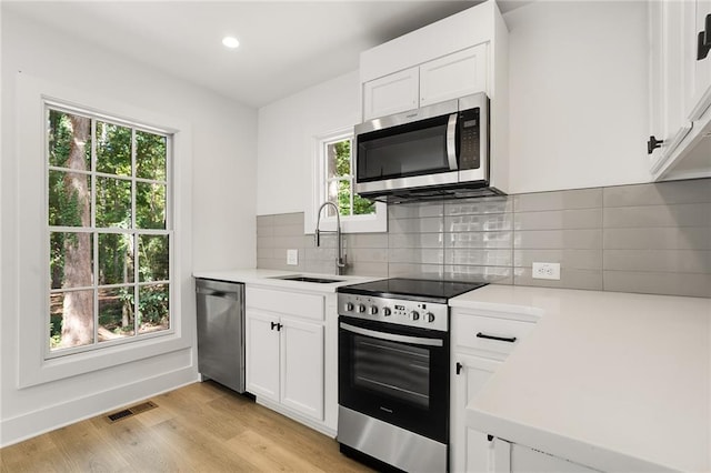 kitchen featuring decorative backsplash, stainless steel appliances, sink, light hardwood / wood-style flooring, and white cabinetry