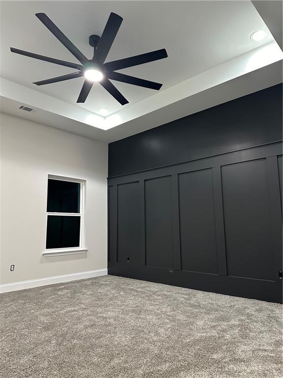 carpeted empty room with ceiling fan, visible vents, a decorative wall, and a raised ceiling