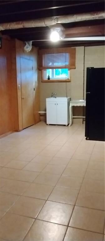 basement featuring light tile patterned floors, white refrigerator, and black fridge