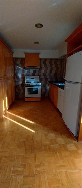 kitchen featuring white fridge, range hood, stainless steel stove, and light parquet floors