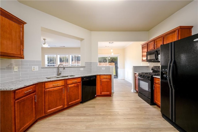 kitchen featuring light stone counters, light wood-style flooring, a sink, black appliances, and tasteful backsplash