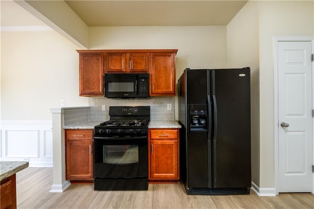 kitchen featuring light stone countertops, a wainscoted wall, light wood-style flooring, black appliances, and backsplash