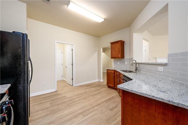 kitchen featuring brown cabinetry, light wood-style flooring, freestanding refrigerator, a sink, and range with gas cooktop