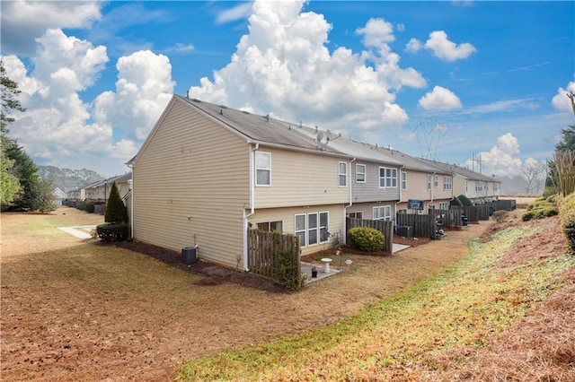 rear view of property with a lawn, central AC unit, and fence