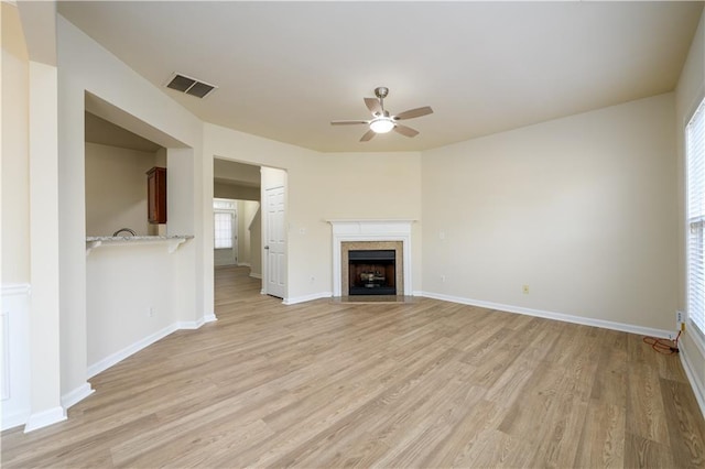 unfurnished living room featuring visible vents, a fireplace with flush hearth, light wood-style floors, baseboards, and ceiling fan