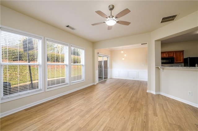 unfurnished living room with visible vents, light wood-style flooring, a ceiling fan, and a wainscoted wall