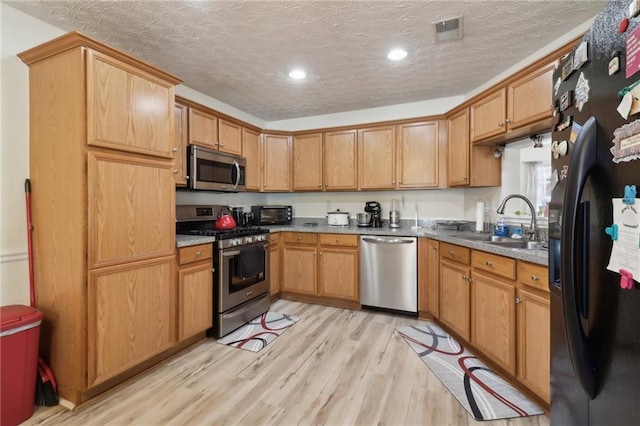 kitchen featuring a textured ceiling, stainless steel appliances, a sink, visible vents, and light wood-type flooring