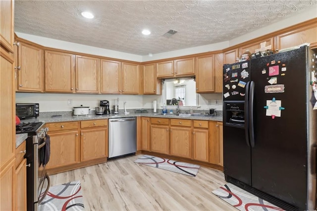 kitchen featuring stainless steel appliances, a sink, a textured ceiling, light stone countertops, and light wood-type flooring