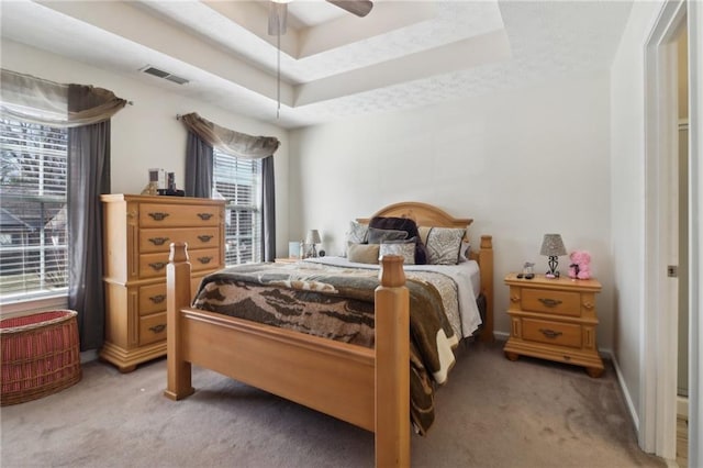 bedroom with light carpet, a tray ceiling, visible vents, and baseboards