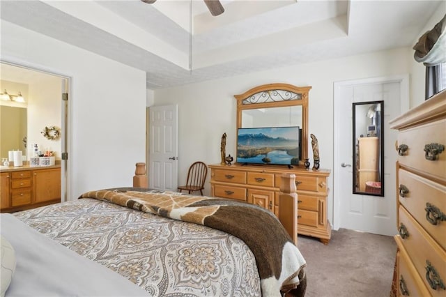 bedroom with light carpet, ceiling fan, a tray ceiling, and ensuite bath