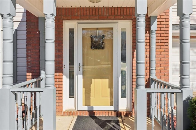 doorway to property featuring a garage, covered porch, and brick siding