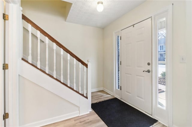 foyer entrance with stairs, a textured ceiling, wood finished floors, and baseboards