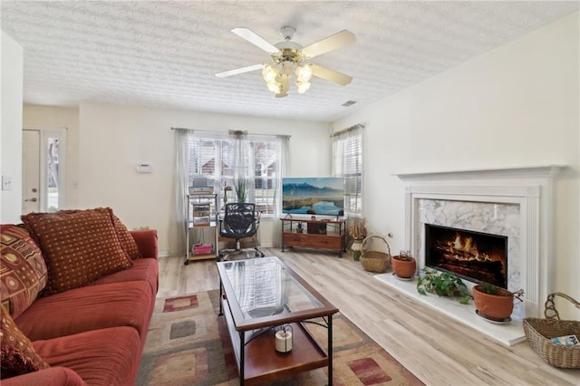 living room with ceiling fan, a fireplace, a textured ceiling, and wood finished floors