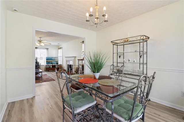 dining room featuring a fireplace, a textured ceiling, baseboards, and wood finished floors