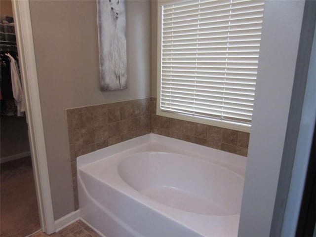 full bath with a walk in closet, a garden tub, and baseboards